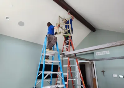 Two men working on a ladder in a bedroom.